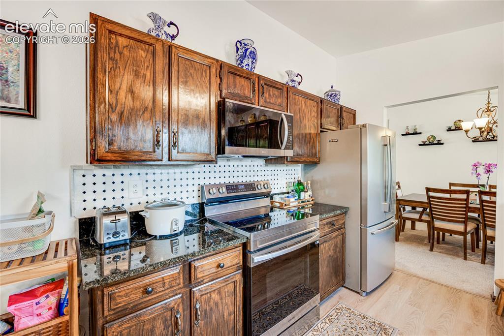 Image 10 of 46: Kitchen featuring wood cabinetry, dark granite countertops, and a white peg
