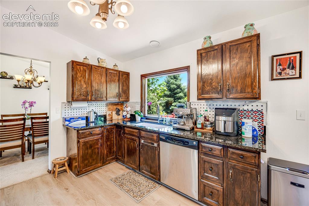 Image 11 of 46: Kitchen featuring wood-finish cabinetry, dark granite countertops, and stai