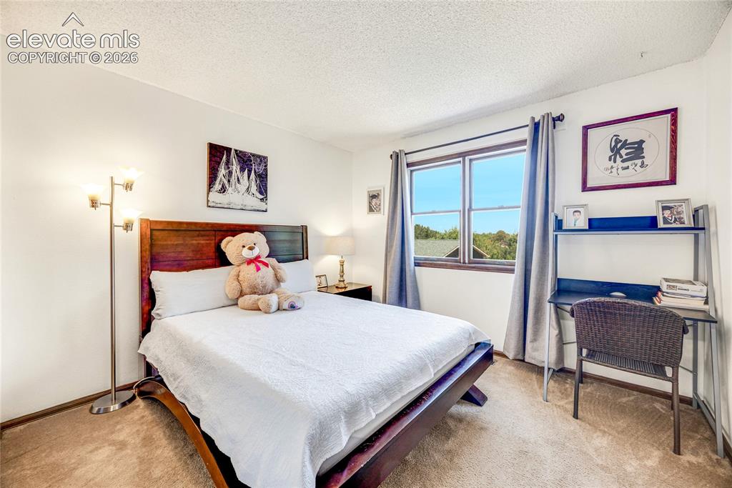 Image 21 of 46: Carpeted bedroom featuring a large window with blue drapes, white walls, an