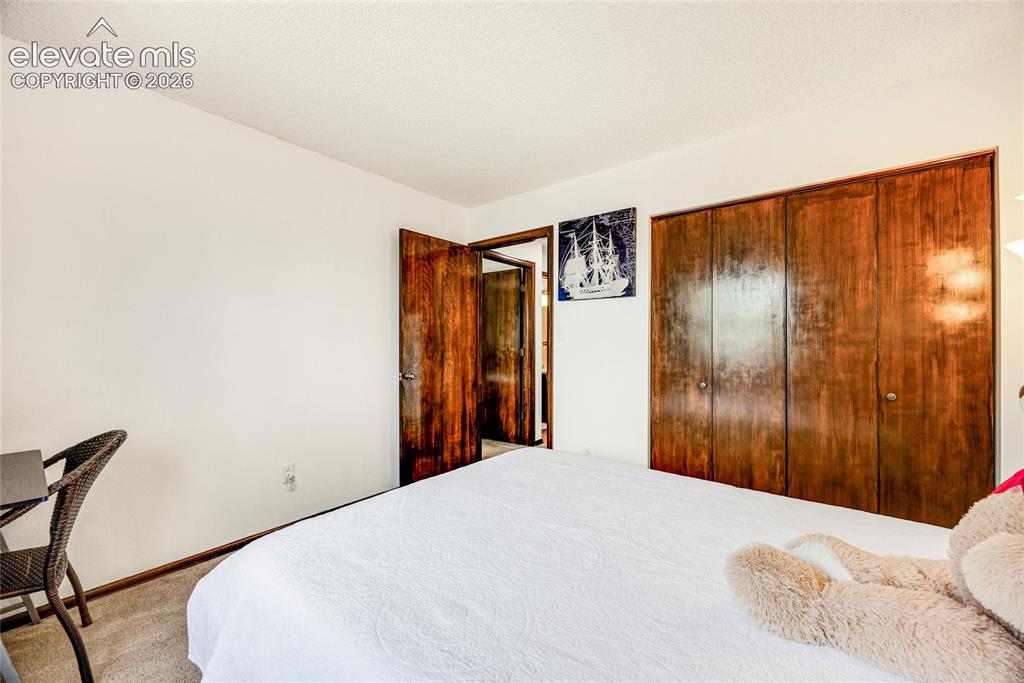 Image 22 of 46: Bedroom featuring light neutral walls, textured ceiling, wood-finish bi-fol