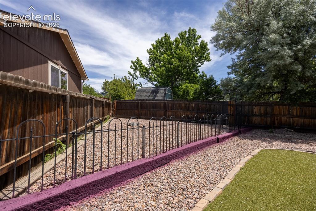 Image 35 of 46: Fenced outdoor space featuring a gravel area, artificial turf, and mature t