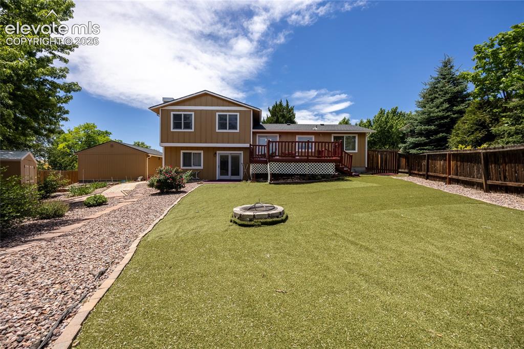 Image 37 of 46: Spacious backyard featuring artificial turf, a rock pathway, a fire pit, a