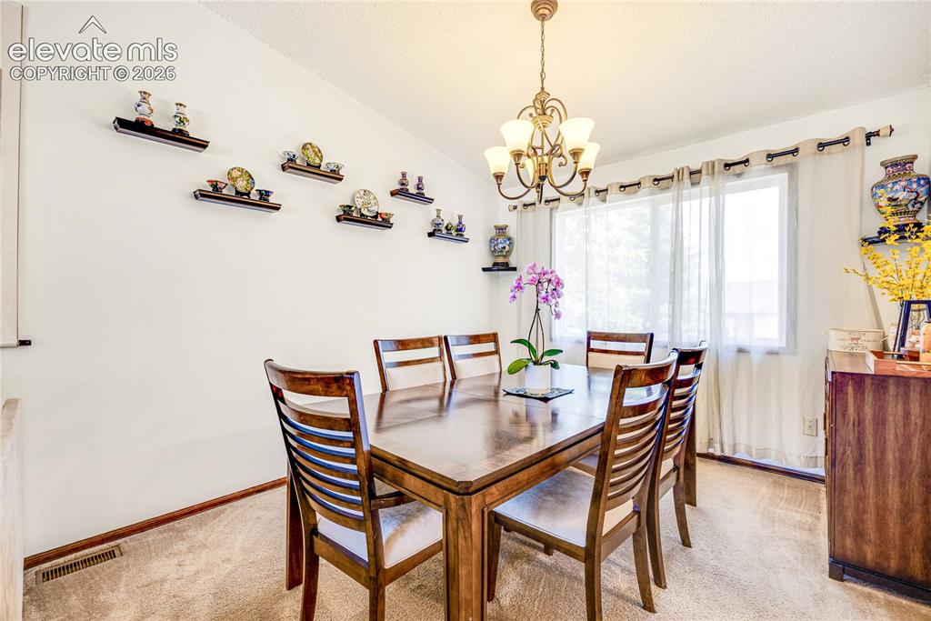Image 8 of 46: Dining area featuring a classic chandelier, a large window with sheer curta