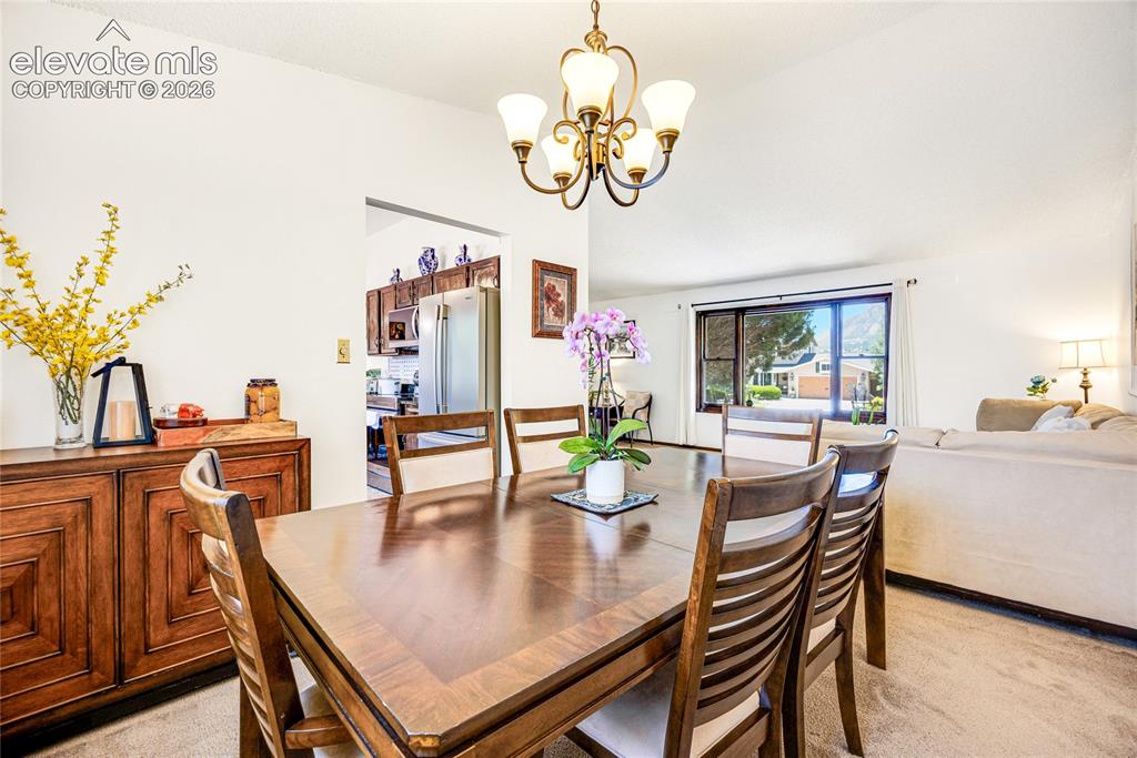 Image 9 of 46: Dining area featuring a vaulted ceiling, chandelier lighting, and a large w