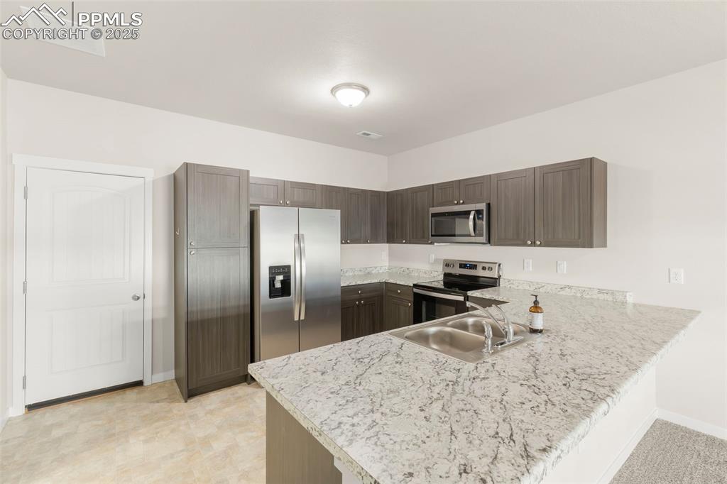 Image 10 of 27: Kitchen with a peninsula, stainless steel appliances, dark brown cabinets, 