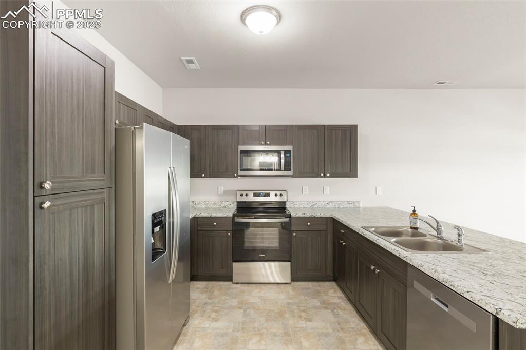 Image 11 of 27: Kitchen with appliances with stainless steel finishes, a peninsula, dark br