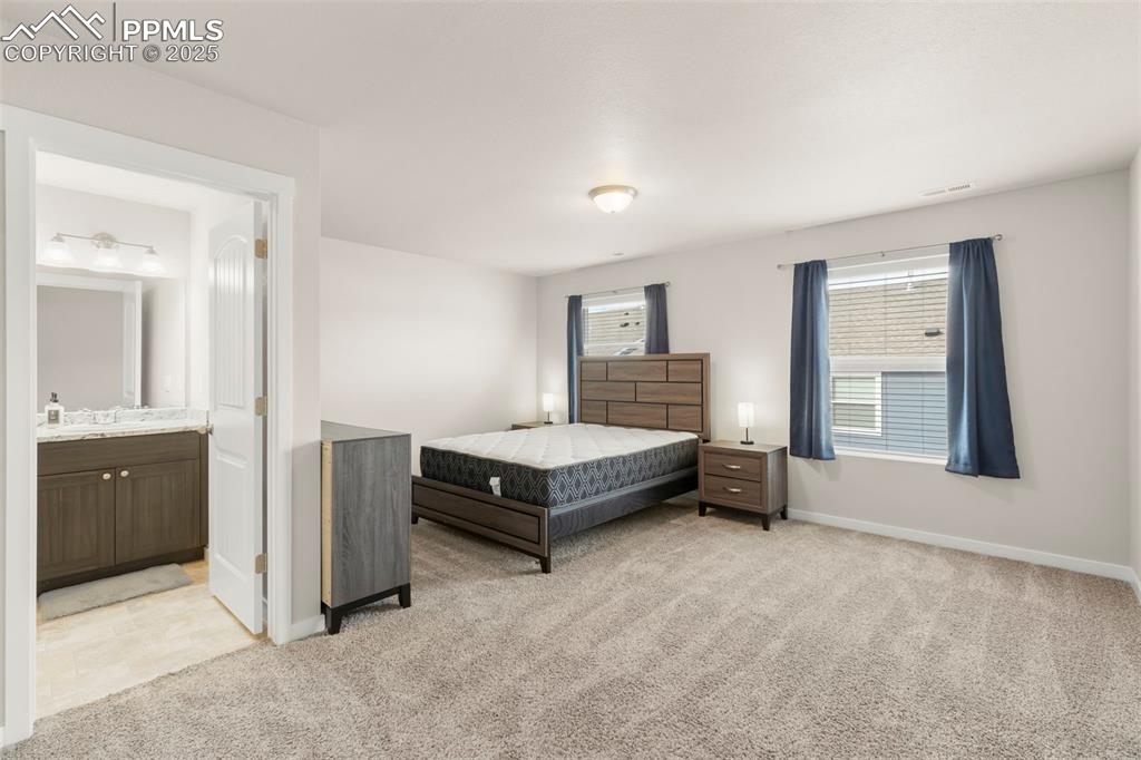 Image 15 of 27: Bedroom with light colored carpet and ensuite bathroom