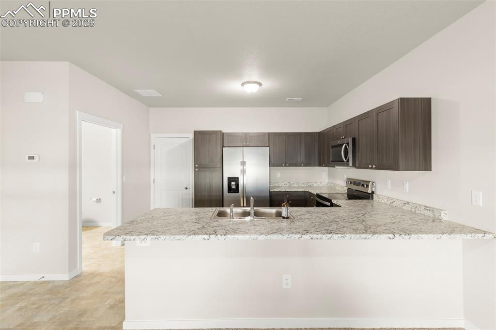 Image 3 of 27: Kitchen featuring stainless steel appliances, a peninsula, dark brown cabin