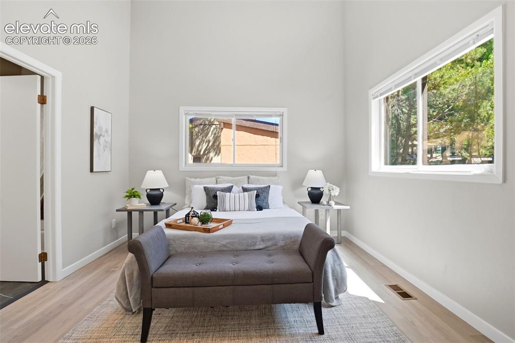 Image 12 of 19: Light-filled bedroom featuring vaulted ceilings, light wood-finish flooring