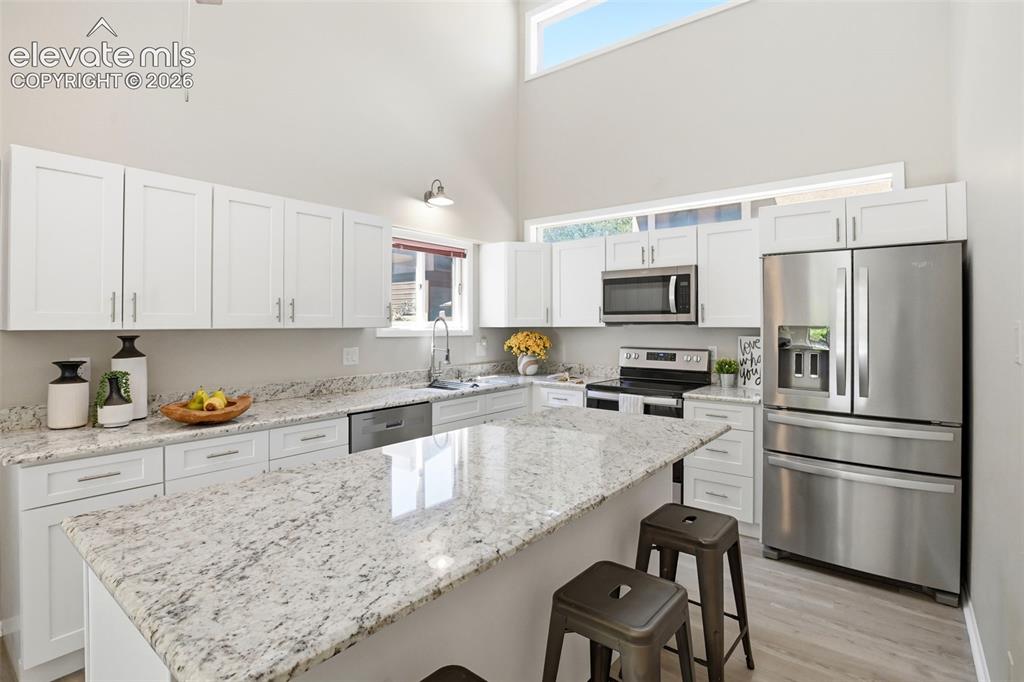 Image 6 of 19: Kitchen featuring a central island with a stone-finish countertop, white ca