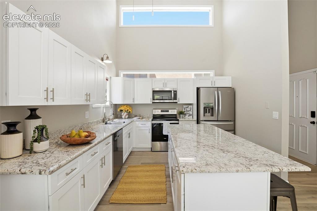 Image 8 of 19: Modern kitchen featuring white cabinetry, light-colored granite countertops