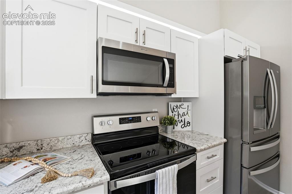 Image 9 of 19: Modern kitchen featuring white flat-panel cabinetry, light granite countert