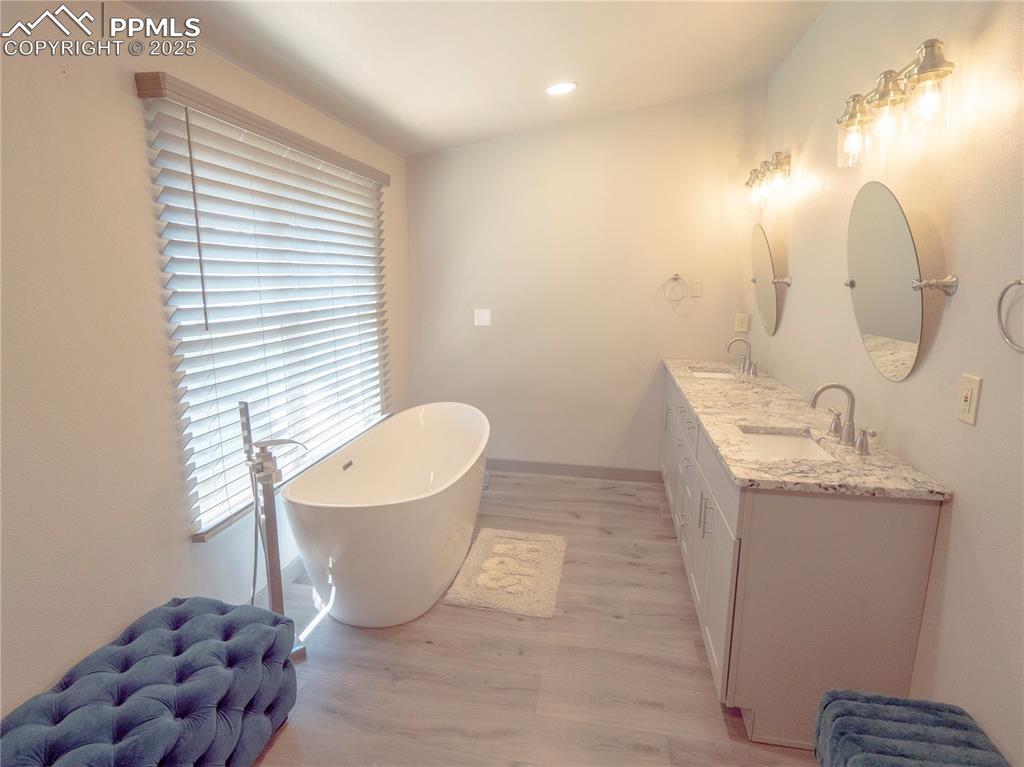 Image 14 of 39: Full bathroom with wood finished floors, a freestanding bath, double vanity