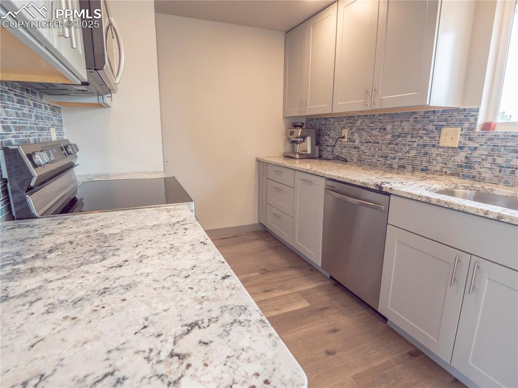 Image 6 of 39: Kitchen featuring backsplash, appliances with stainless steel finishes, lig