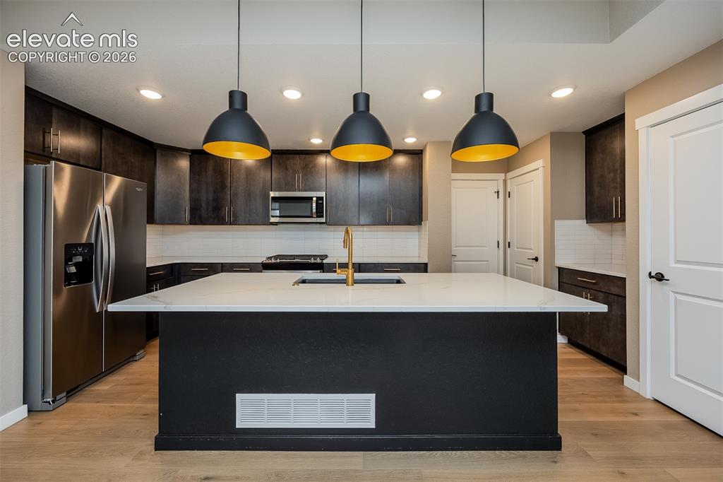 Image 26 of 40: Kitchen featuring a large central island with a white countertop and a gold