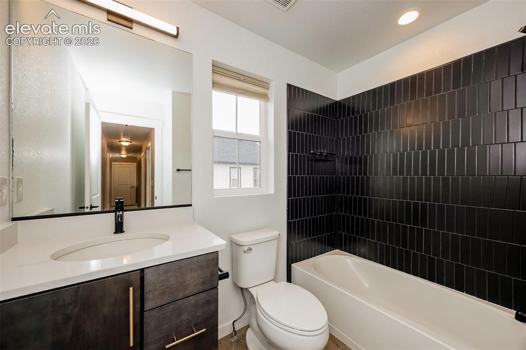 Image 38 of 40: Bathroom featuring a white bathtub with dark subway tile surround, white co