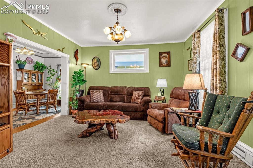 Image 4 of 30: Carpeted living area with a chandelier, baseboard heating, and crown moldin
