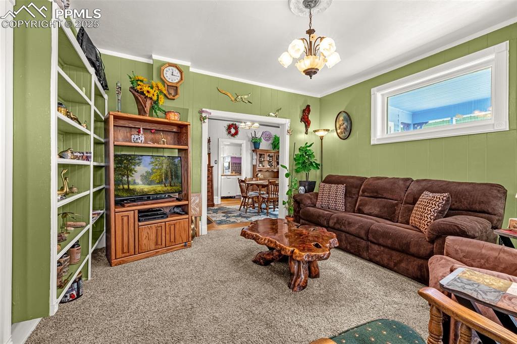 Image 5 of 30: Living area with a chandelier, carpet, and ornamental molding