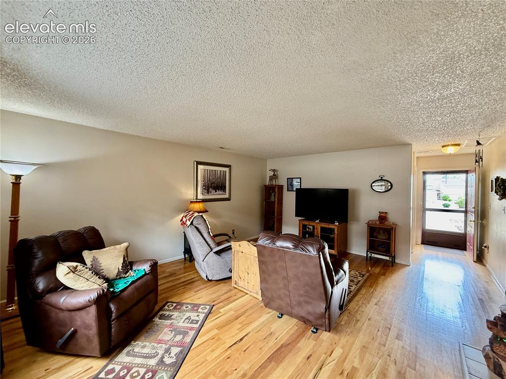 Image 10 of 26: Living room with wood finished floors, a textured ceiling, and baseboards