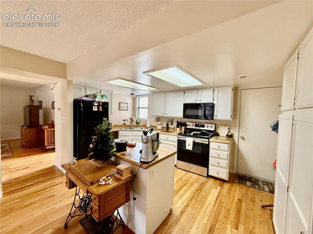 Image 3 of 26: Kitchen with black appliances, light wood-style floors, white cabinets, a t