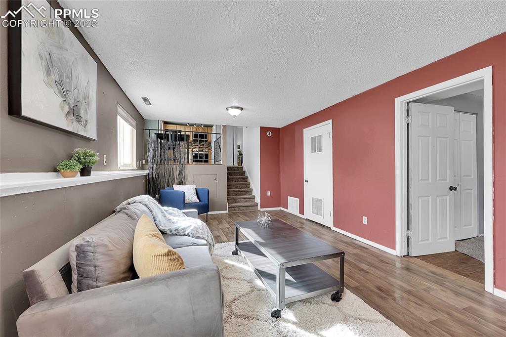 Image 12 of 36: Living area with wood finished floors, a textured ceiling, and stairs