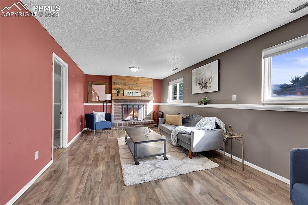 Image 4 of 36: Living area with a brick fireplace, wood finished floors, a textured ceilin