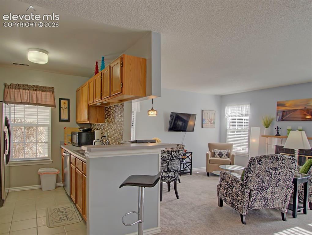 Image 11 of 13: Open-concept living space featuring a kitchen with wood cabinetry and tile 