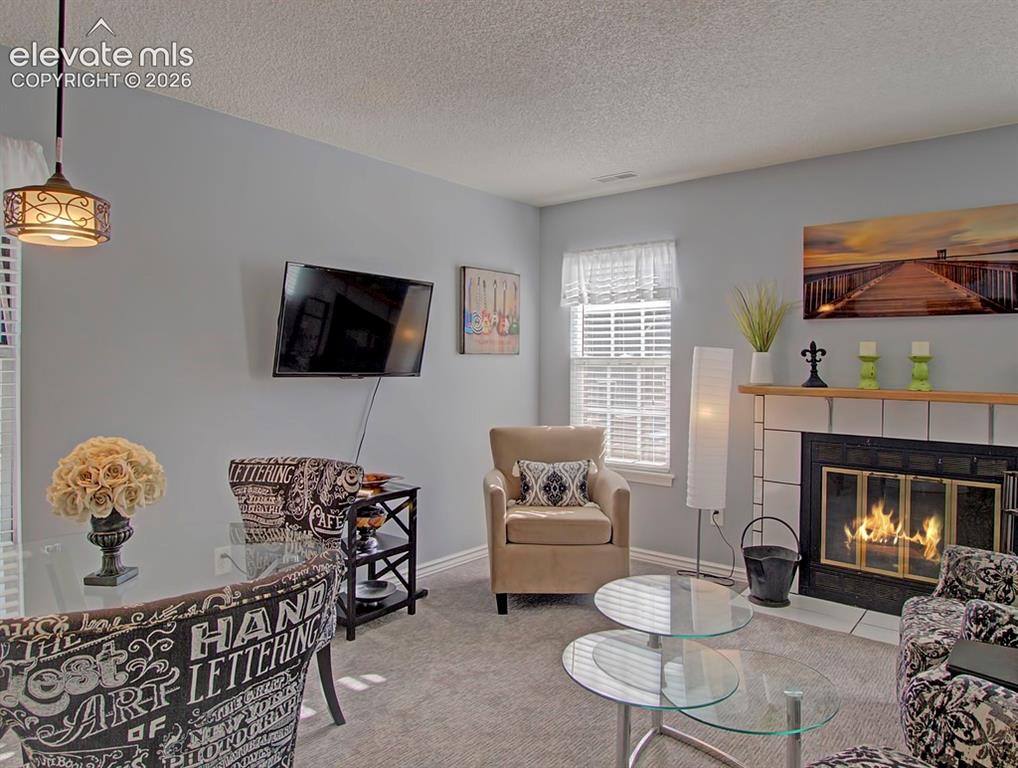 Image 9 of 13: Living area featuring a fireplace with a tile surround and wood mantel, lig