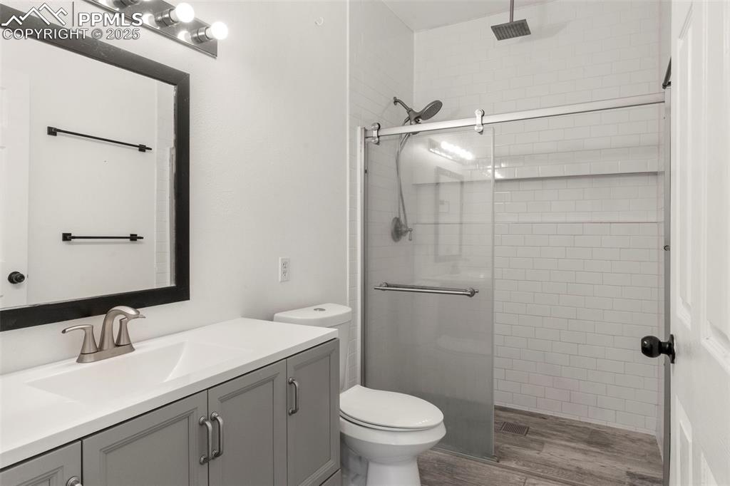 Image 12 of 15: Bathroom featuring a tile shower, wood finished floors, and vanity