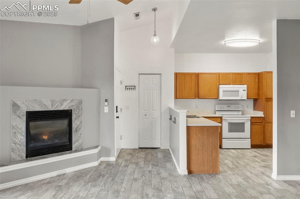 Image 4 of 15: Kitchen with white appliances, a towering ceiling, brown cabinetry, light c
