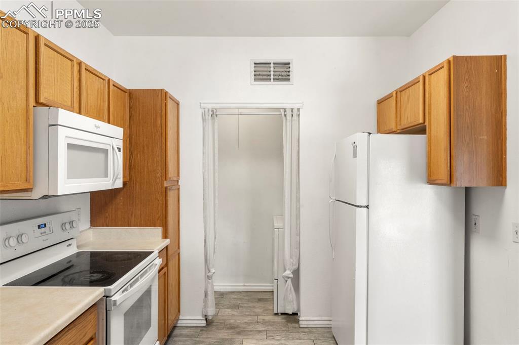 Image 6 of 15: Kitchen with white appliances, light wood-style floors, light countertops, 