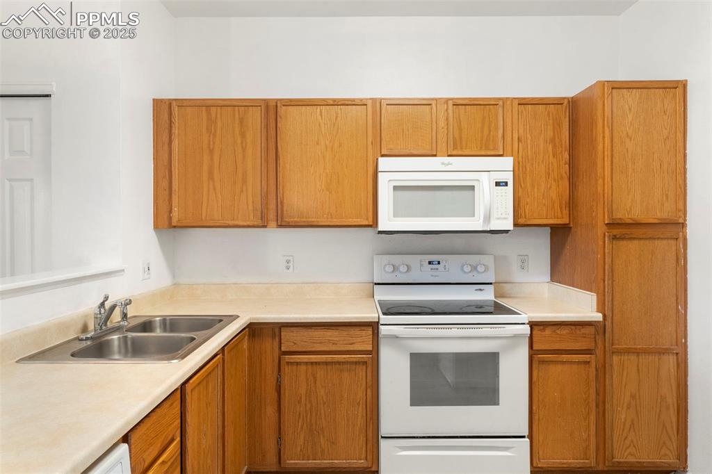 Image 8 of 15: Kitchen featuring white appliances, light countertops, and brown cabinets