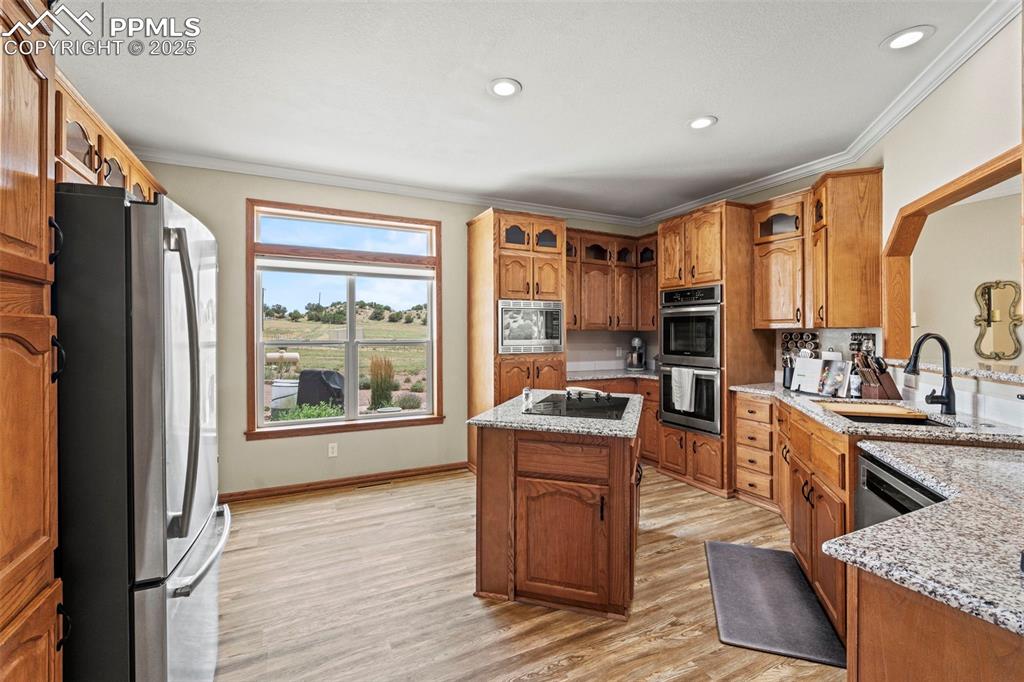 Image 20 of 41: Kitchen with stainless steel appliances, brown cabinetry, light wood-style