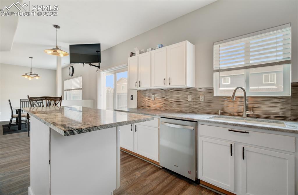Image 8 of 35: Kitchen with white cabinetry, backsplash, dishwasher, light stone counters,