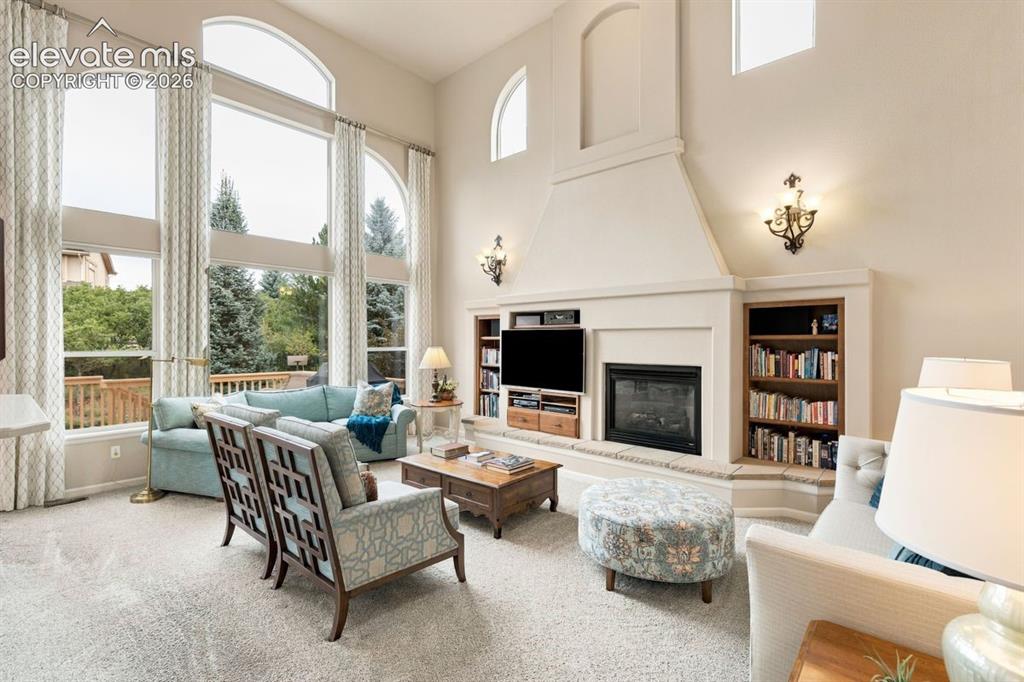 Image 3 of 50: Grand family room with a wall of windows, fireplace, and ceiling fan