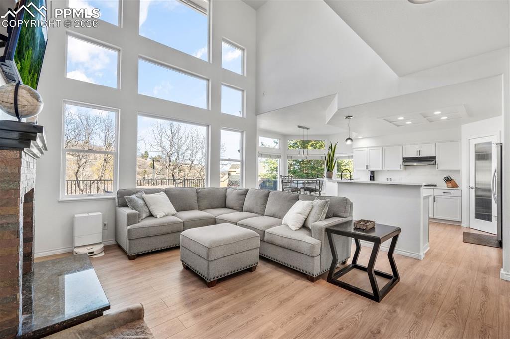Image 10 of 49: Living area with light wood-style flooring, a fireplace, and a high ceiling