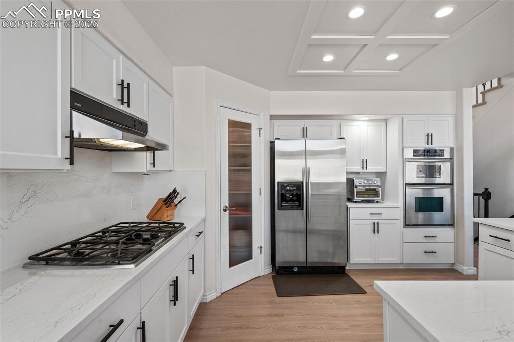Image 14 of 49: Kitchen with stainless steel appliances, white cabinetry, light wood-type f
