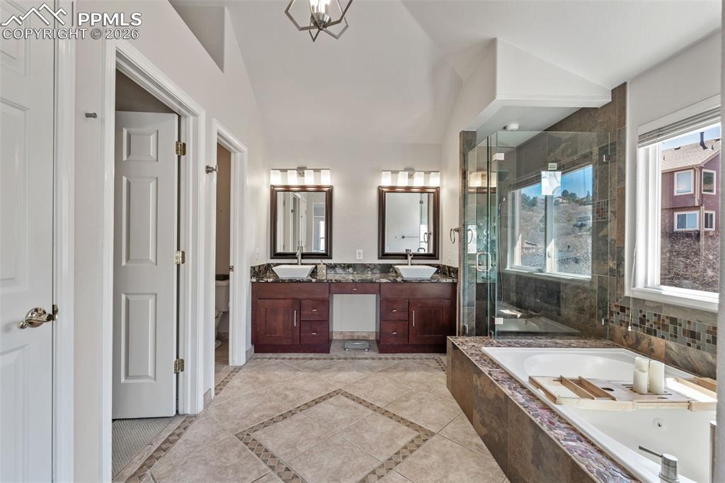 Image 27 of 49: Bathroom featuring double vanity, a stall shower, a bath, lofted ceiling, a