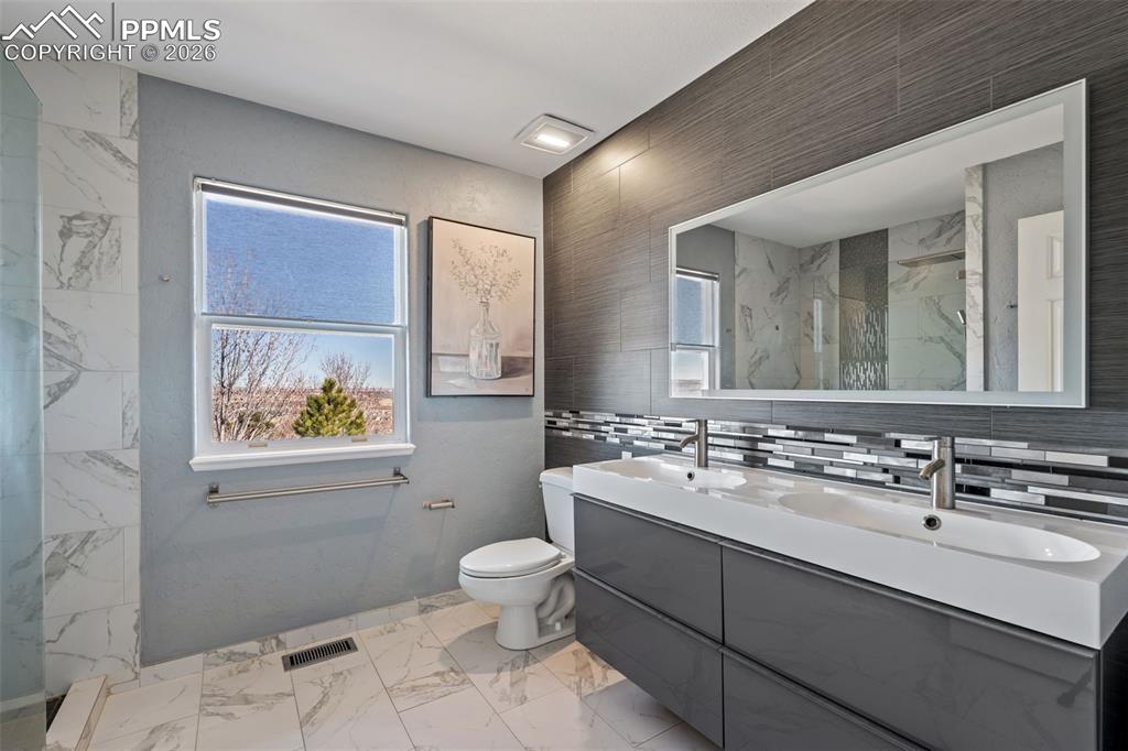 Image 31 of 49: Full bath featuring double vanity, plenty of natural light, light marble fi