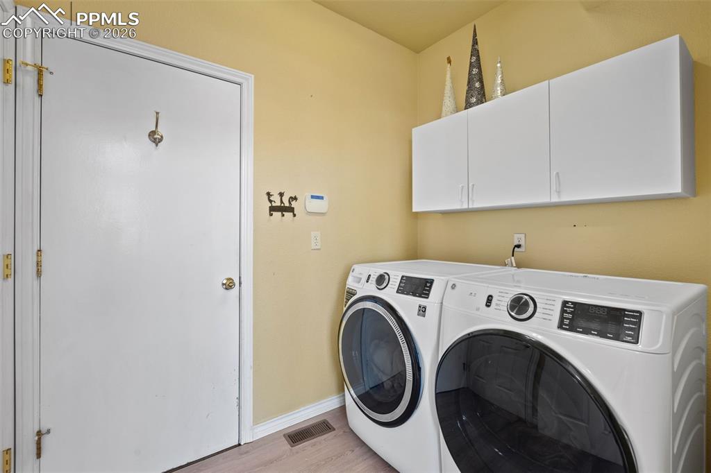 Image 41 of 49: Laundry area featuring independent washer and dryer, cabinet space, and lig