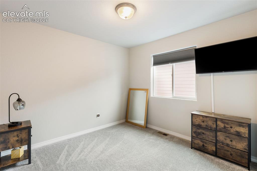 Image 18 of 28: Bedroom featuring a window with a roller shade, light-colored carpeting, a 