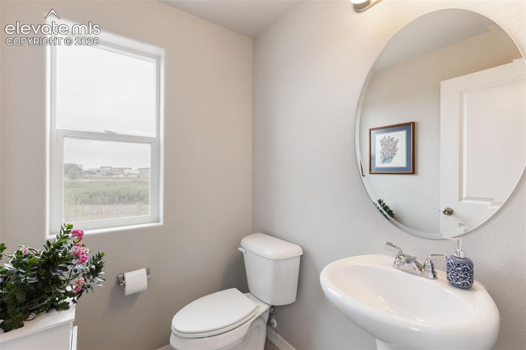 Image 21 of 28: Neutral wall tones with a window, a toilet, and a pedestal sink featuring a