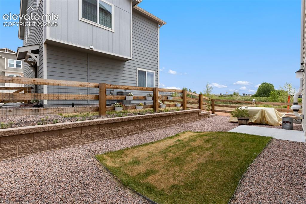 Image 23 of 28: Tiered backyard featuring a retaining wall, a split-rail fence, and gravel 