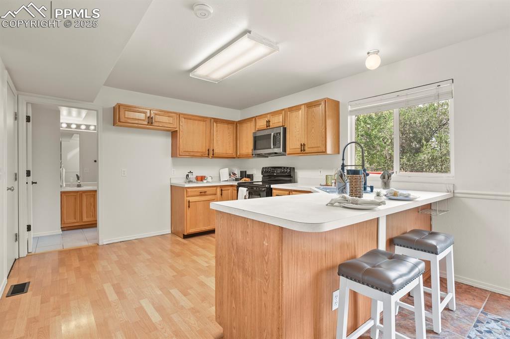 Image 12 of 45: Kitchen with a peninsula, light countertops, black electric range, stainles