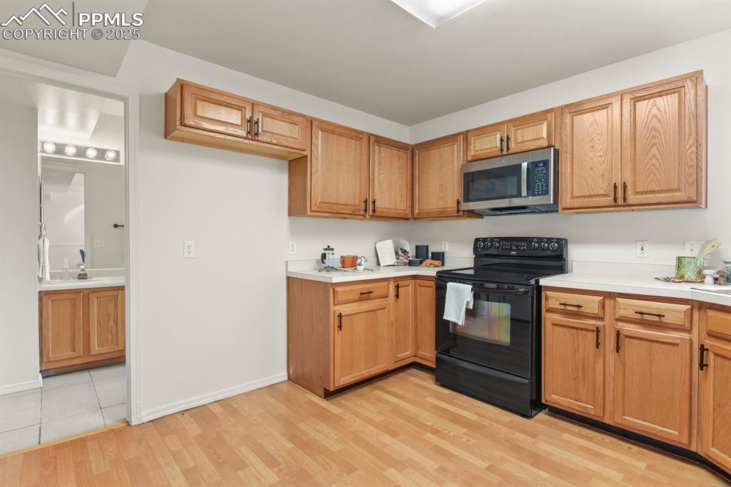 Image 14 of 45: Kitchen with black range with electric stovetop, stainless steel microwave,