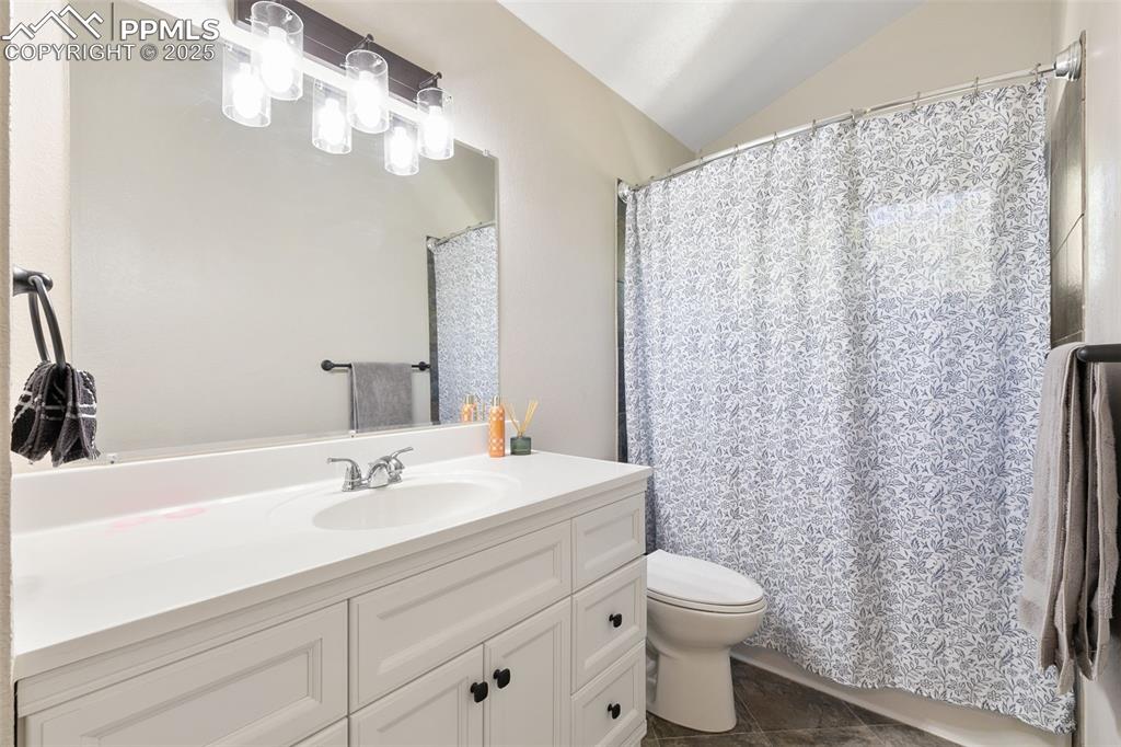 Image 22 of 29: Bathroom with vanity, lofted ceiling, dark tile patterned floors, and curta