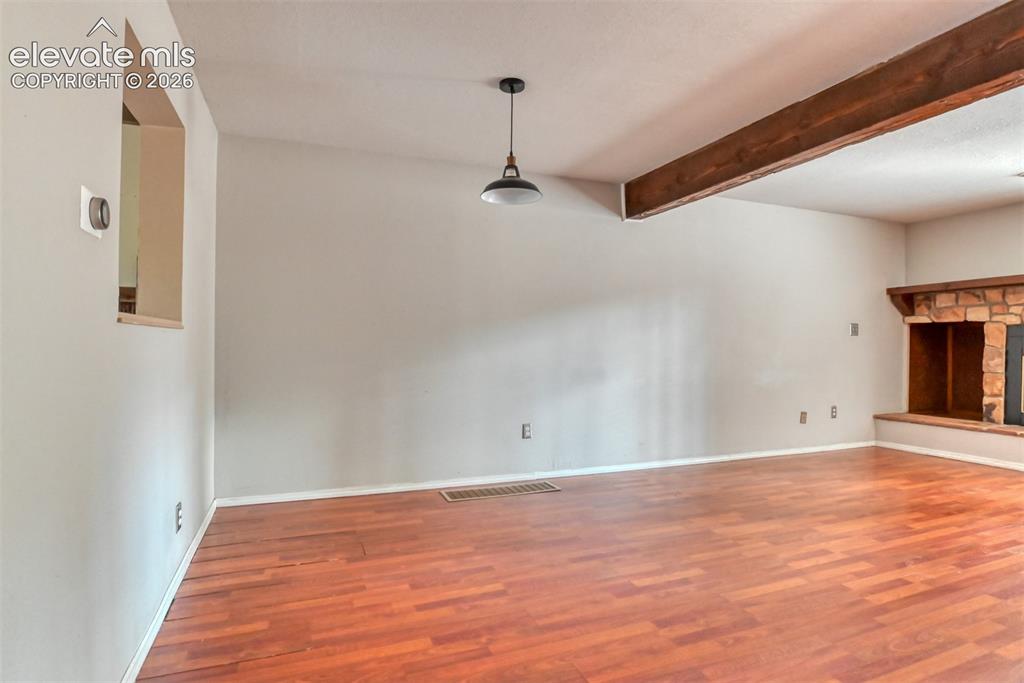 Image 11 of 50: Wood-finish flooring with a stone fireplace, exposed ceiling beam, and susp