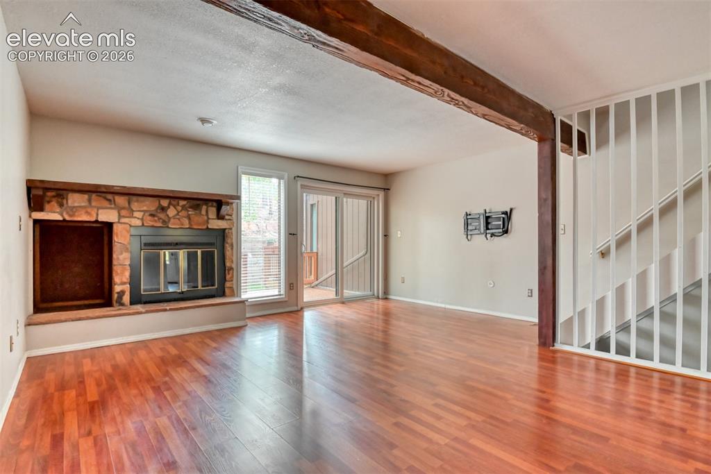 Image 15 of 50: Stone-faced fireplace, wood-finish flooring, exposed wood beam, sliding gla