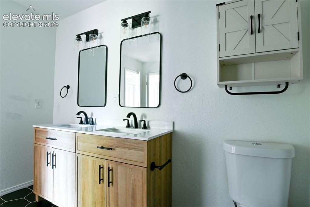 Image 27 of 50: Dual vanity with wood-finish cabinetry, white countertop, and matte black f