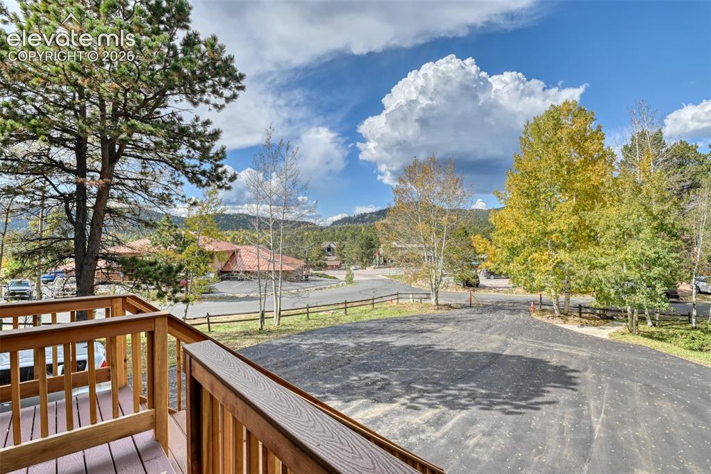Image 4 of 50: Wooden deck with natural wood railing, asphalt paving, and mature trees